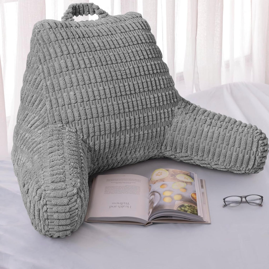 Gray backrest pillow on a bed with an open book and glasses nearby
