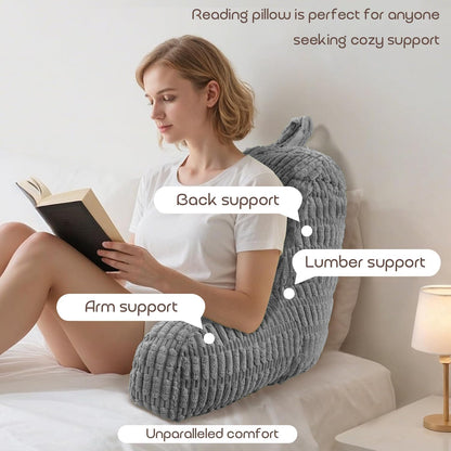 Woman reading a book with a gray reading pillow providing back, arm, and lumber support.