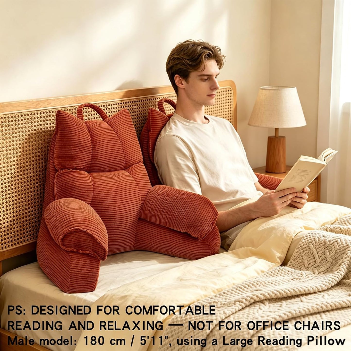 A man sits on a bed reading a book, supported by a large rust-orange ribbed reading pillow shaped like a chair. The scene is a warm bedroom with a cane-embossed headboard, bedside lamp, cream bedding, and overlaid text explaining the product's use.