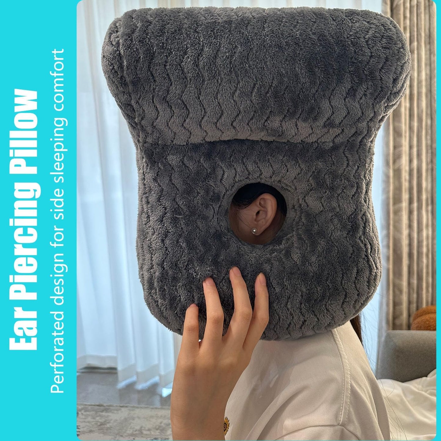 A person wearing a dark gray textured ear piercing pillow with a circular cutout for the ear, shown in a bedroom setting with a turquoise text banner on the left.